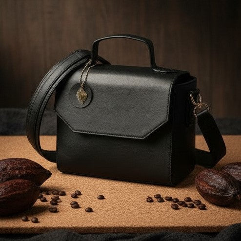 Asteria black plant-based leather crossbody bag shown in side angle on a textured surface with coffee beans, highlighting structured design and sustainable material