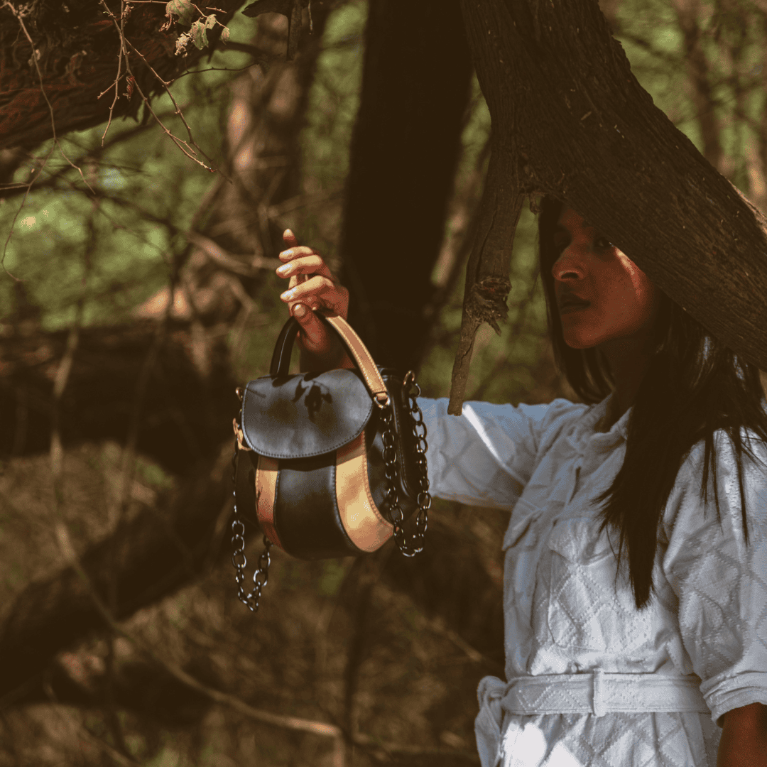 Aurora black and gold plant-based leather sling bag held by a woman outdoors in natural forest setting