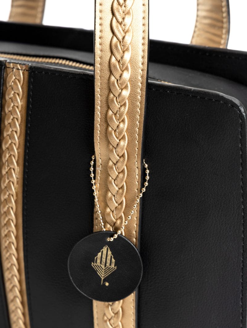 Gaia black and gold plant leather shoulder bag close-up showing braided handles and signature logo charm detail