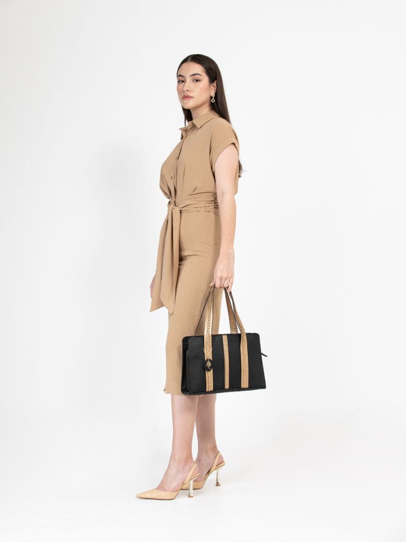 Model holding Gaia black and gold plant leather shoulder bag, showcasing size and carry style in a studio setting