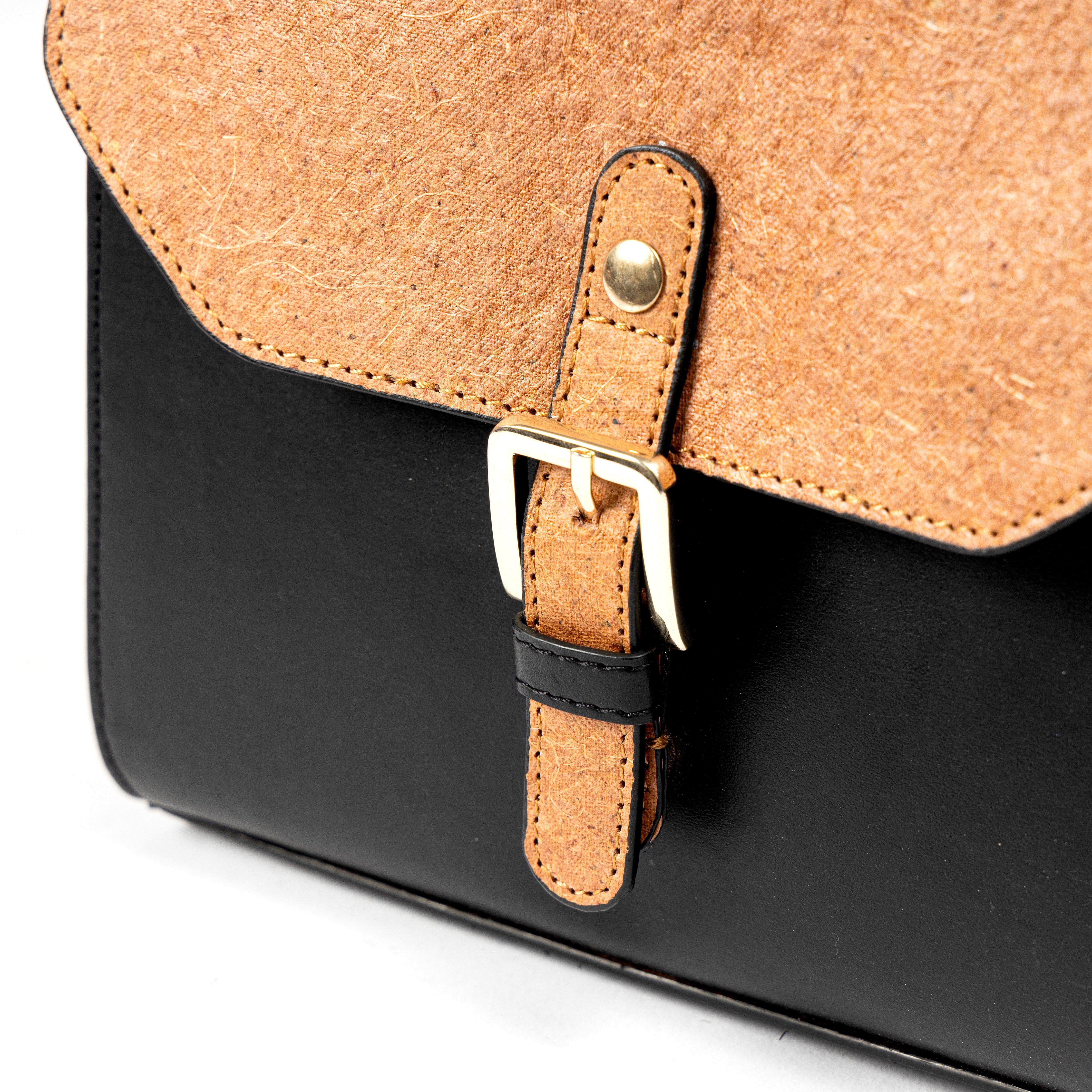 Close-up of buckle closure detail on black and coconut orange plant leather sling bag with gold hardware