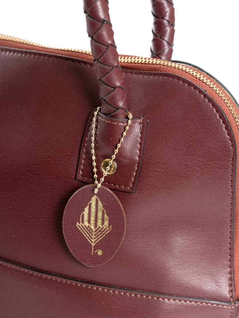 Close-up of Theia red plant-based leather shoulder bag showing textured material, braided handle, and Green Hermitage logo tag
