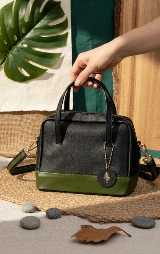 Vanadey plant leather satchel crossbody bag in black and green held by hand with natural textured background and leaf elements