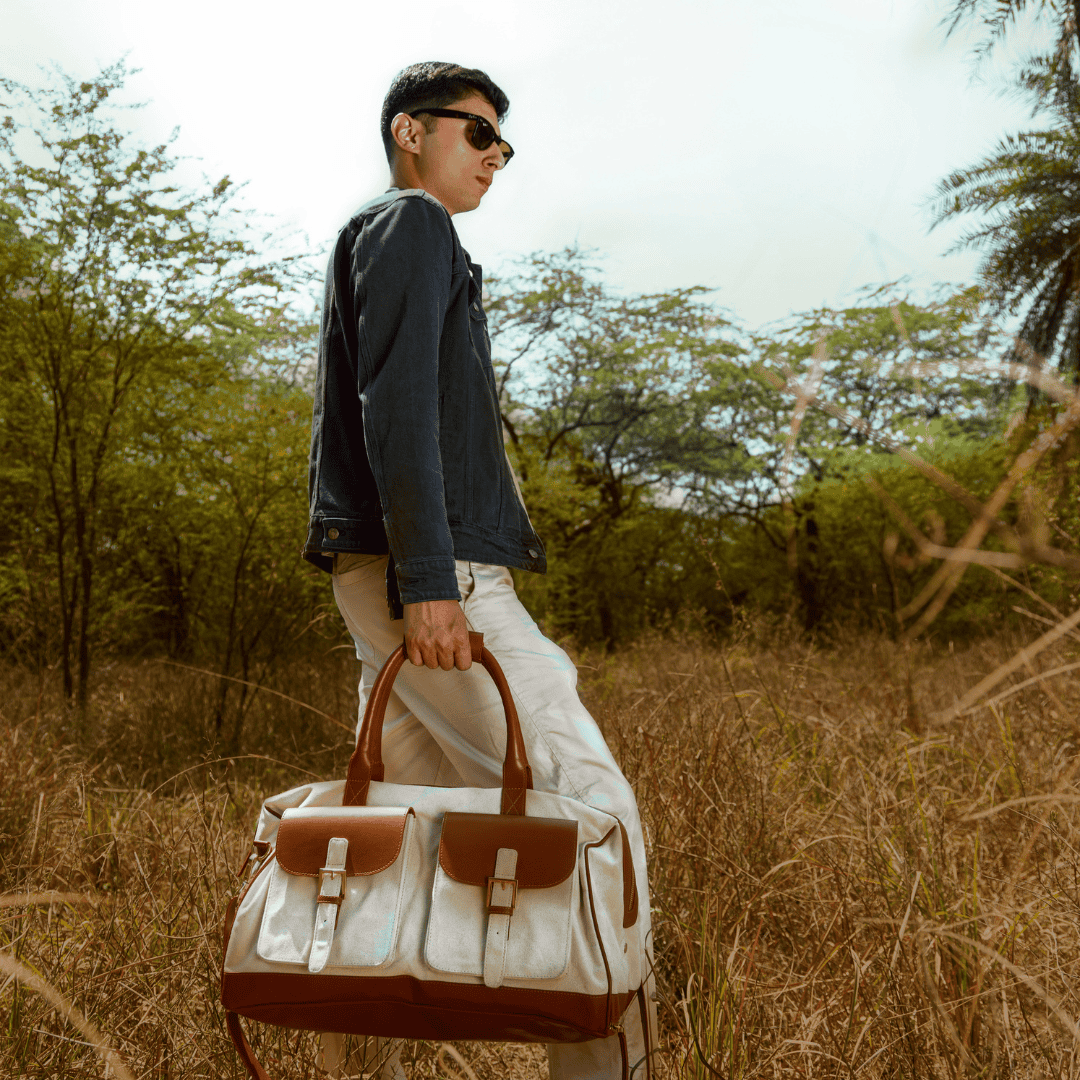 Man carrying Ajax plant leather duffle bag in beige and gingerbread colour outdoors, showcasing travel-ready design in a natural setting