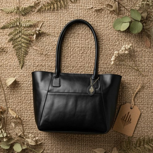 Athena black plant-based leather tote bag on textured surface with natural elements highlighting sustainable materials