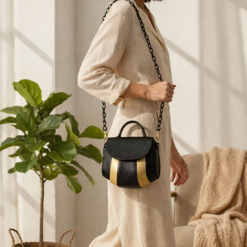Aurora black and gold plant-based leather sling bag worn by a woman indoors with minimal home setting