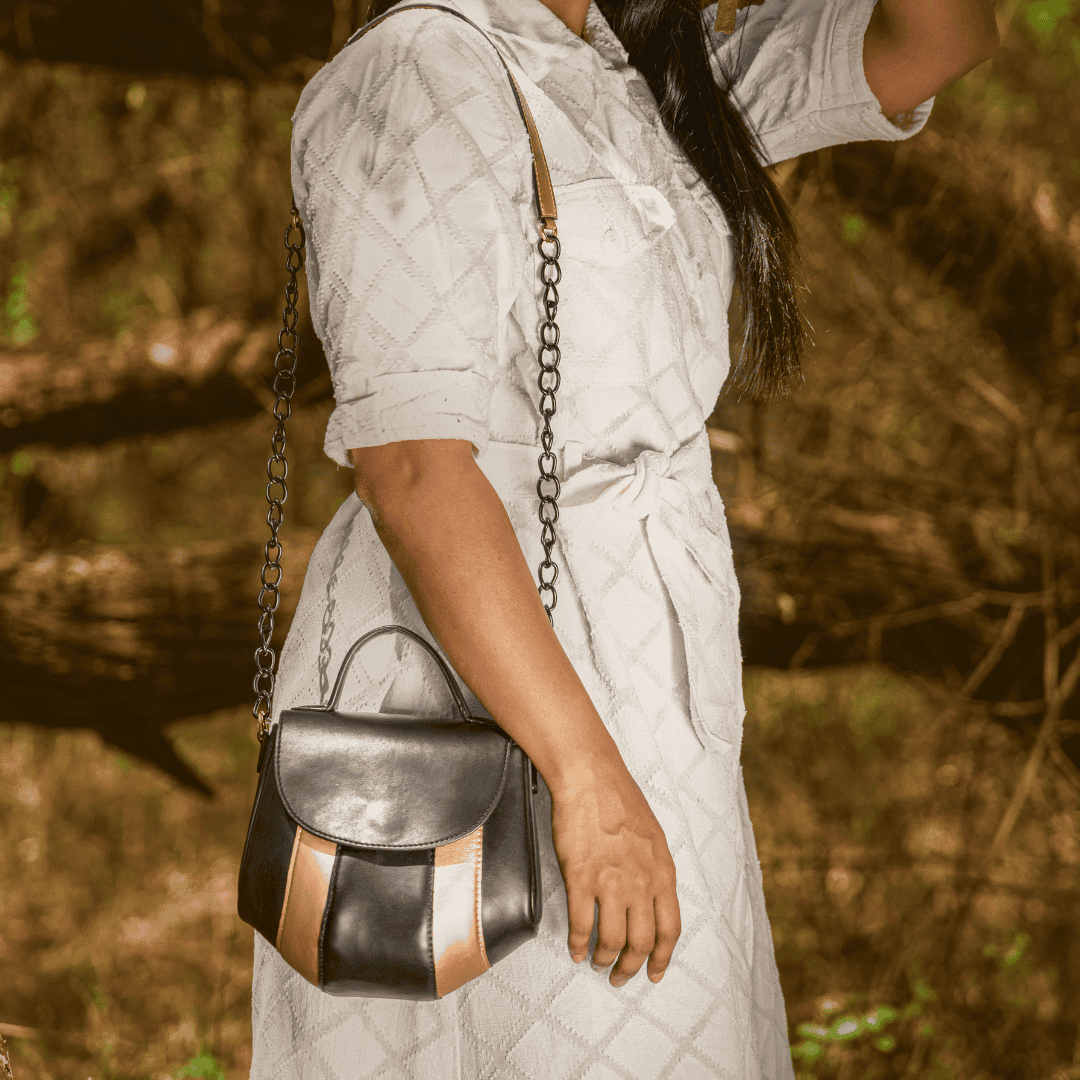 Aurora black and gold plant-based leather sling bag worn crossbody by a woman in an outdoor setting
