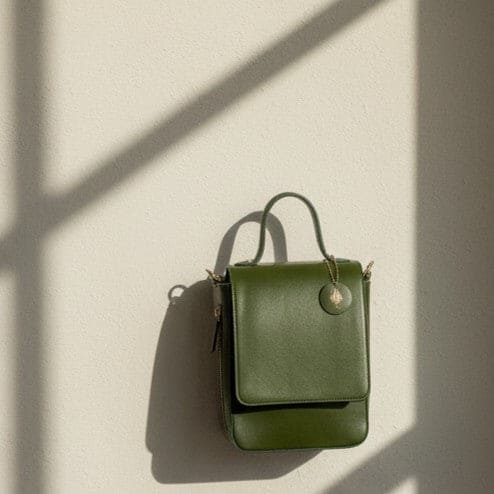 Ceres green plant leather crossbody bag placed against a light beige wall with natural shadows highlighting its structured design