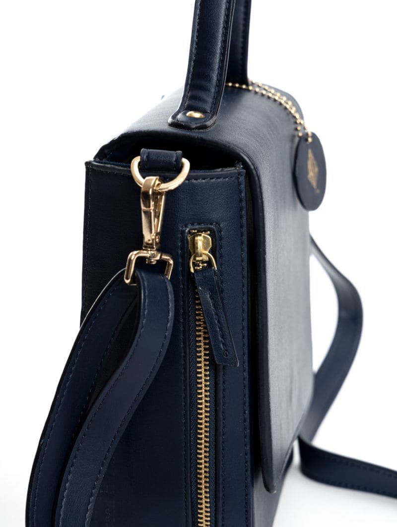 Close-up of Ceres navy blue plant-based leather crossbody bag showing gold hardware, zipper and strap attachment detail