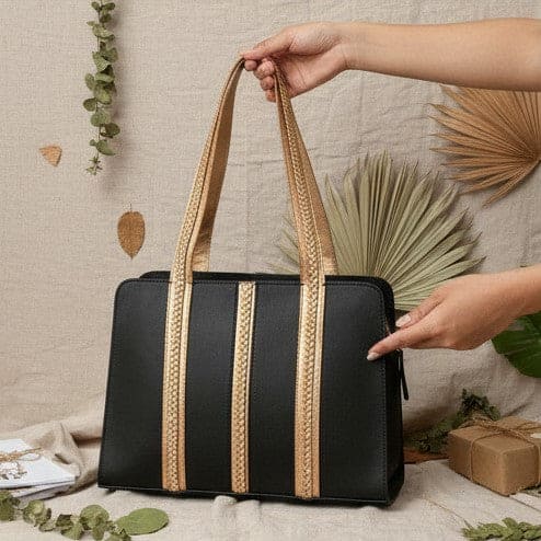 Gaia black and gold plant leather shoulder bag with braided handles, shown being held in a lifestyle setting with natural elements