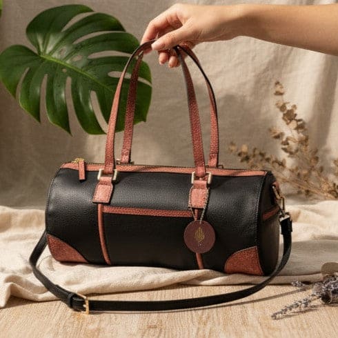 Hand holding the Salacia plant leather bowler bag in black and madder red, handcrafted from fairtrade canvas, cactus leather and malai leather with a detachable shoulder strap.
