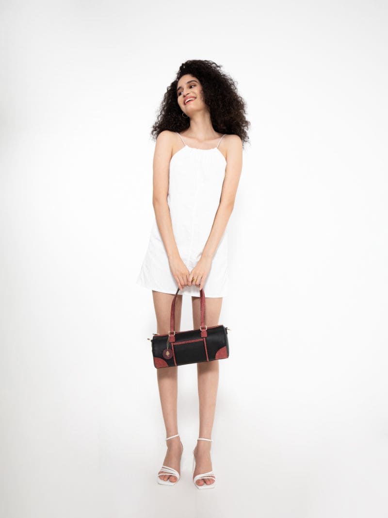 Model holding the Salacia plant leather bowler bag in black and madder red by the top handles, handcrafted from fairtrade canvas, cactus leather and malai leather.