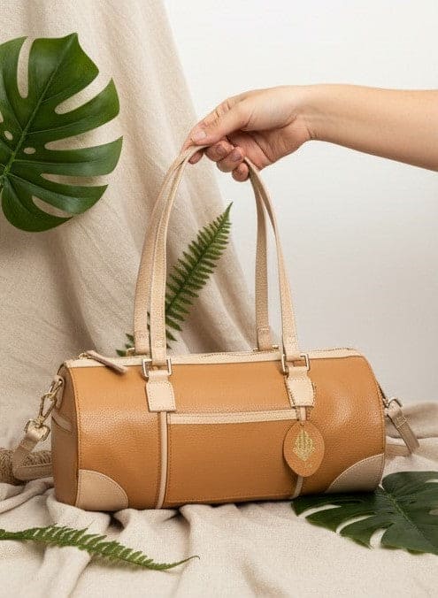 Hand holding the Salacia plant leather bowler bag in caramel and almond with botanical accents, showcasing the lightweight design and handcrafted plant-based apple leather construction.