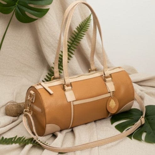 Salacia plant leather bowler bag in caramel and almond displayed in a natural lifestyle setting with botanical accents, handcrafted from fairtrade canvas with plant-based apple leather details.