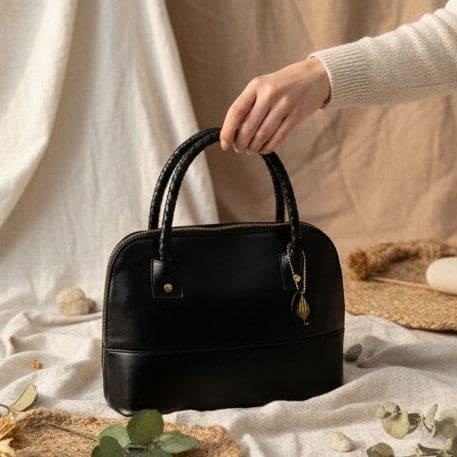 Hand holding Theia black vegan leather shoulder bag showcasing structured silhouette and premium finish in a soft neutral setting