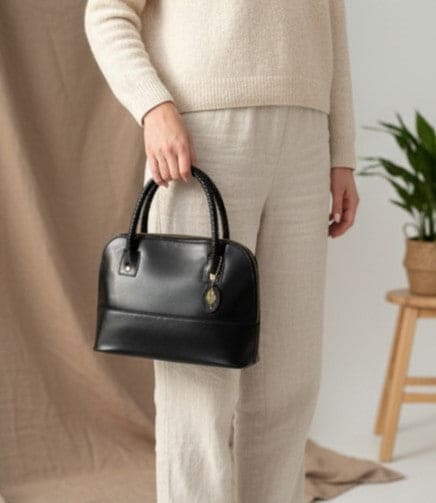 Woman holding Theia black vegan leather shoulder bag in a lifestyle setting highlighting minimal design and everyday elegance